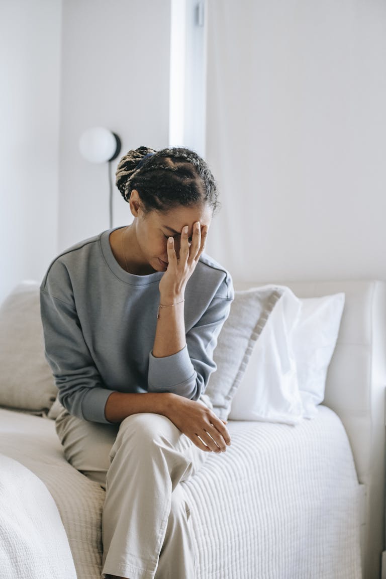 Young unhappy black woman touching face while sitting with crossed legs on bed at home