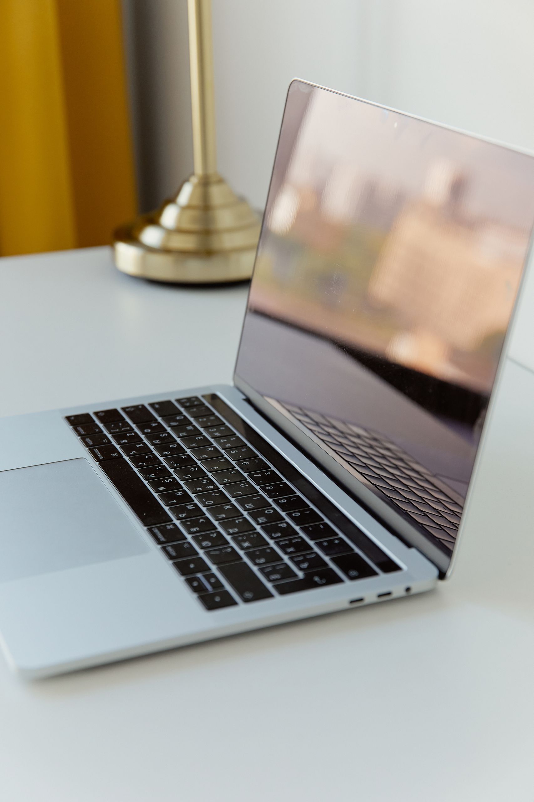 A modern laptop on a white desk with a brass lamp, minimalistic and sophisticated.