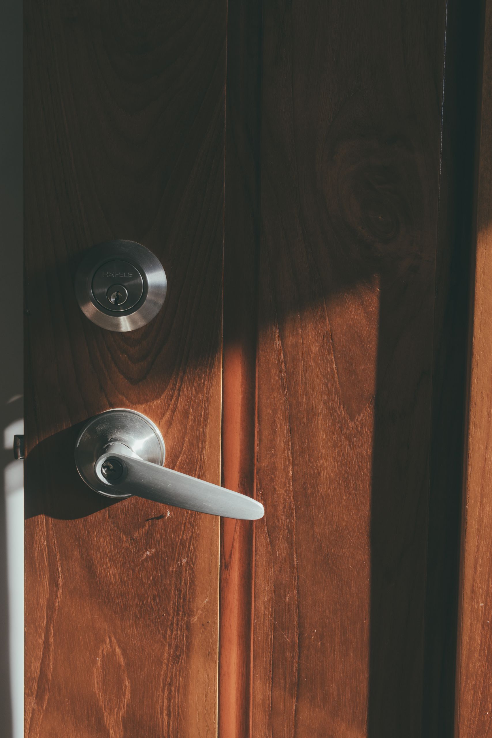 Close-up of a wooden door with a metal handle and warm sunlight casting shadows.