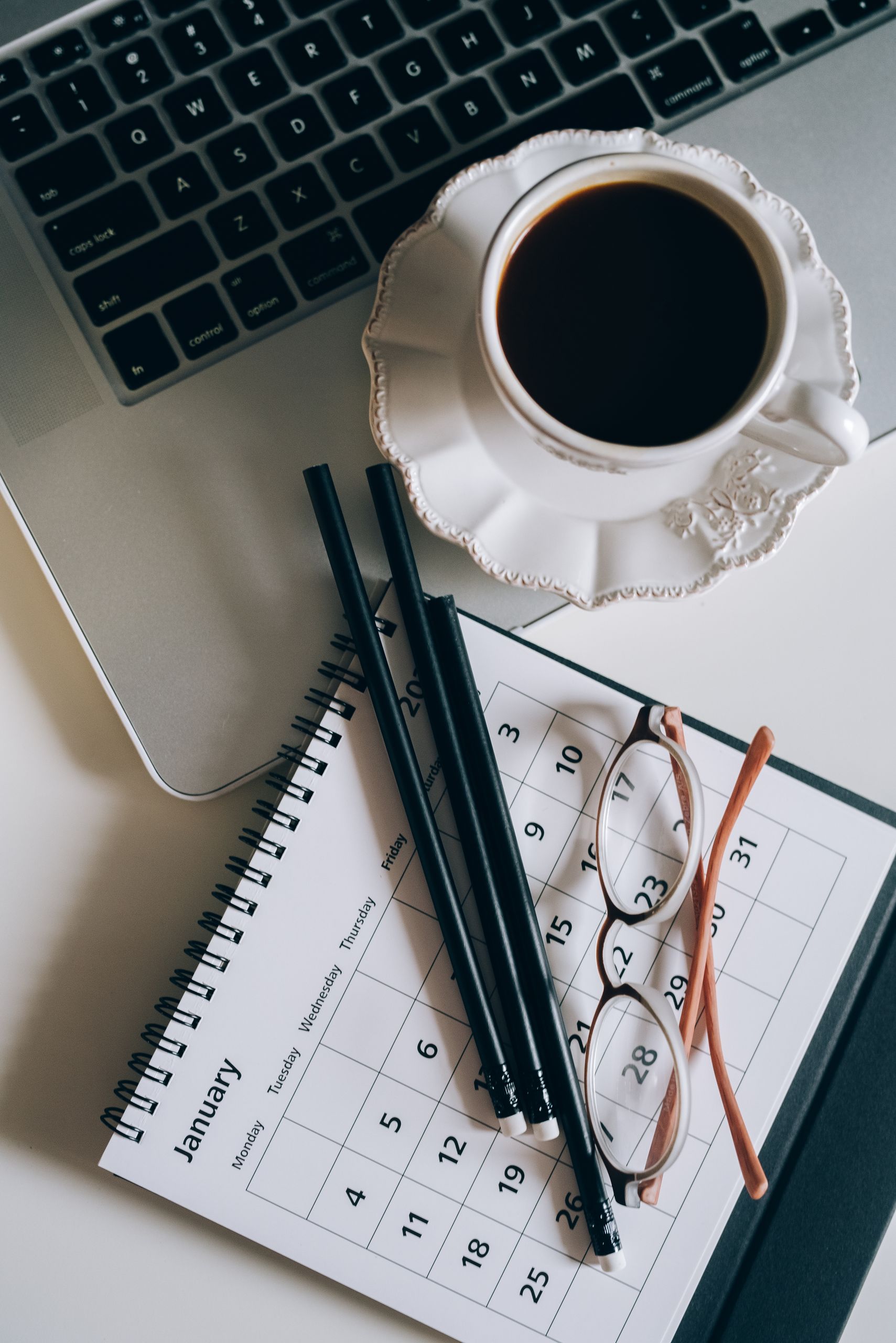Flat lay of a coffee cup, calendar, and laptop for a productive workspace setup.