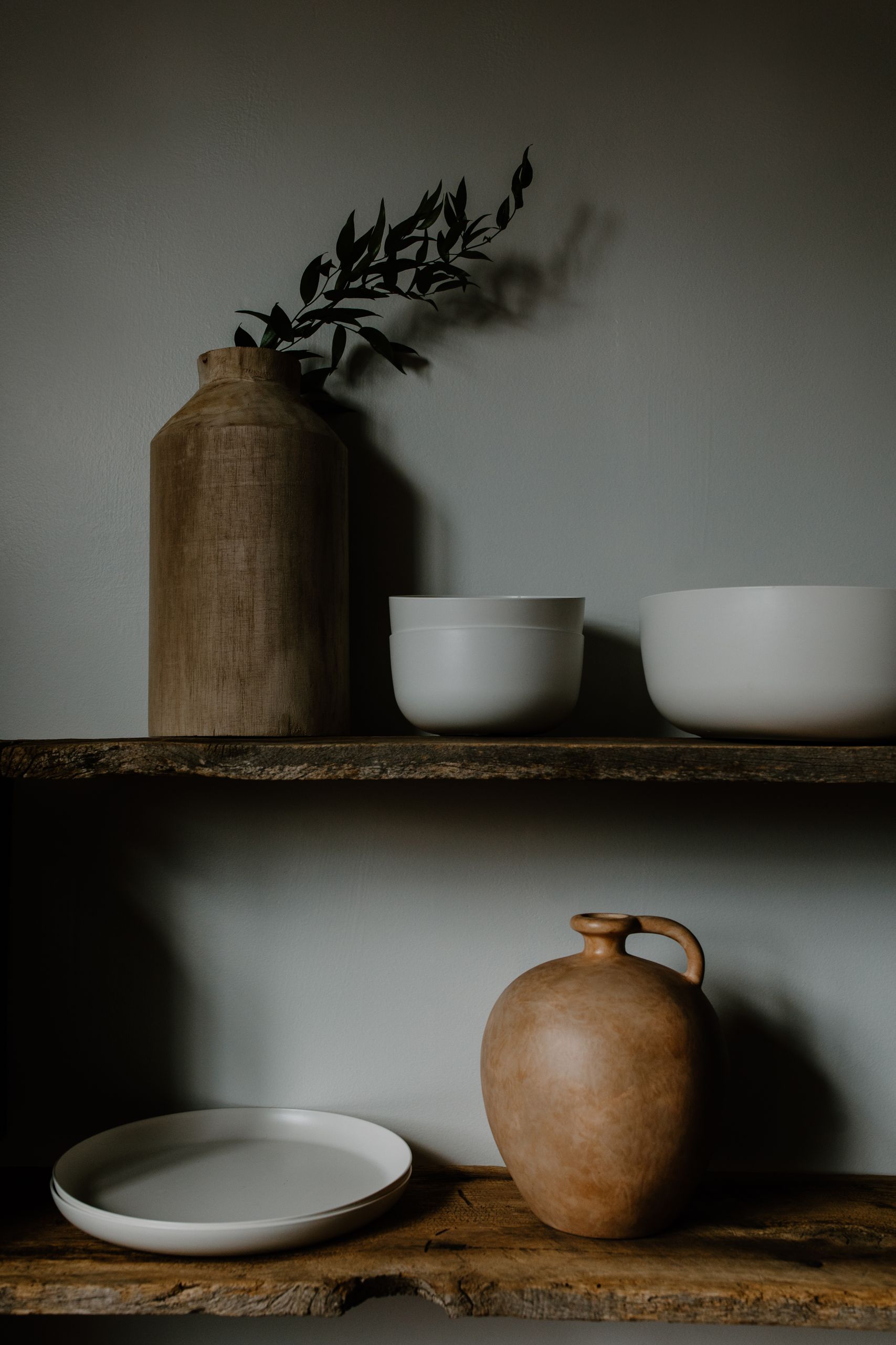 Minimalist display of ceramics and vases on rustic wooden shelves in neutral tones.